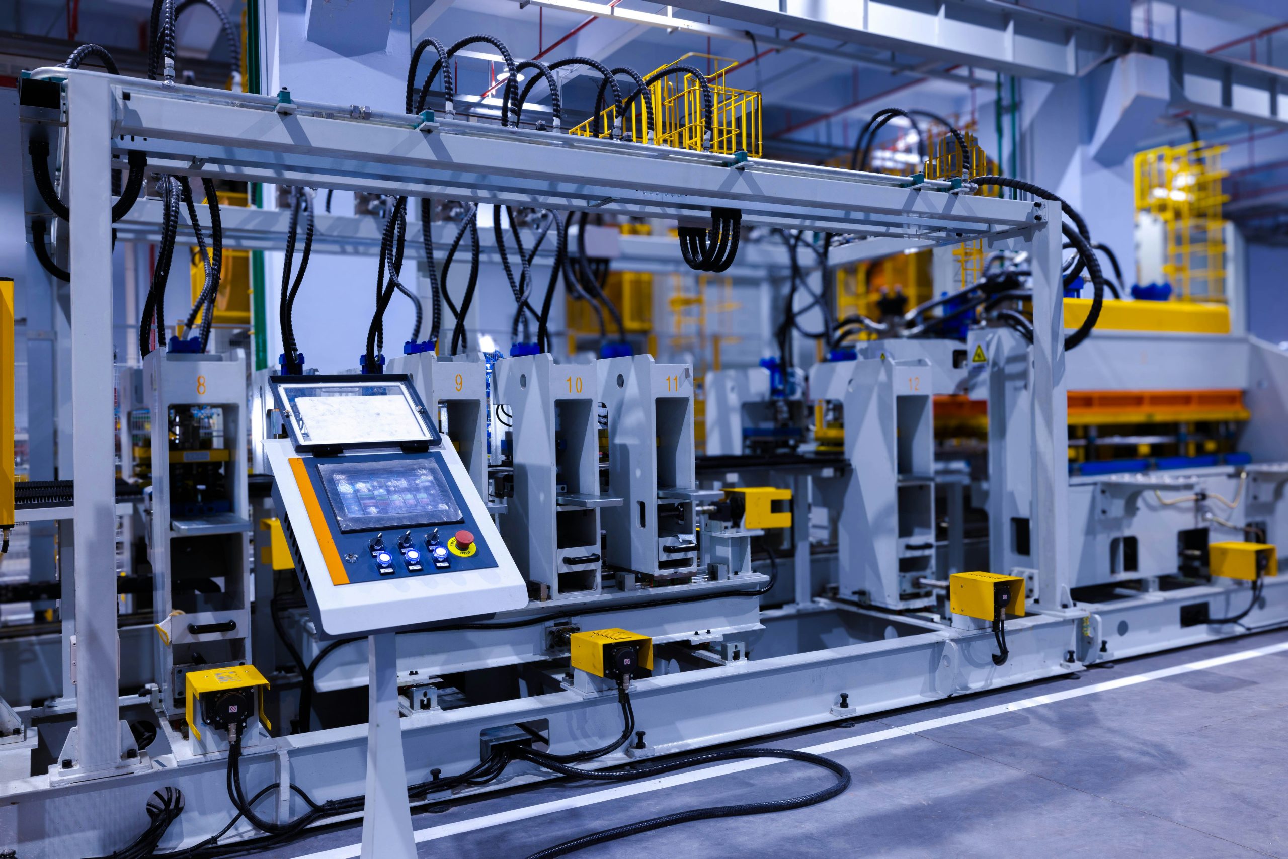 Automated industrial machinery with a control panel in the foreground, featuring several numbered stations connected by cables, within a modern factory setting.