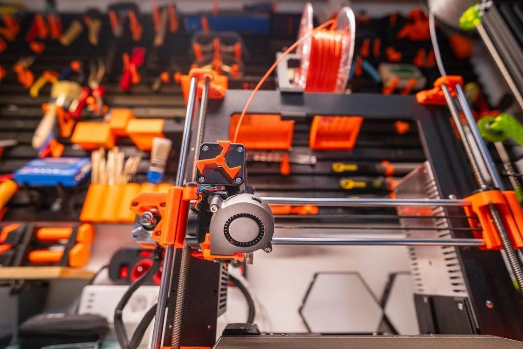Close-up of 3D printer with orange filament and engineering tools in the background
