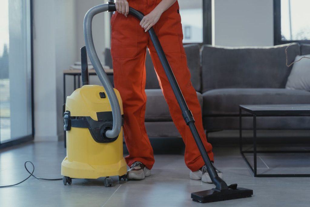 A woman in red overalls uses an industrial vacuum, highlighting efficient home care appliances for deep cleaning.